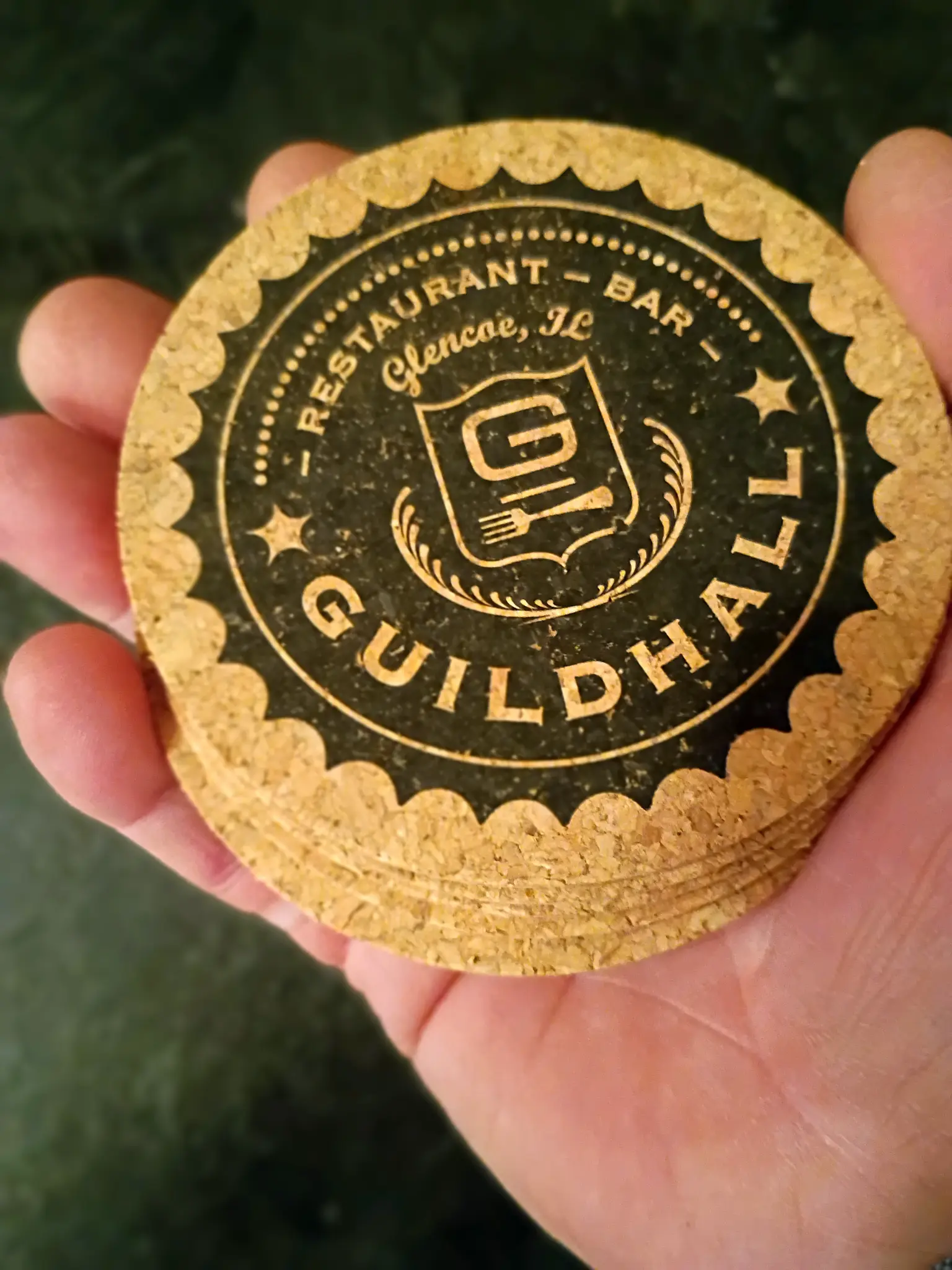 Hand holding premium Guildhall cork coaster with forest background showing quality and craftsmanship